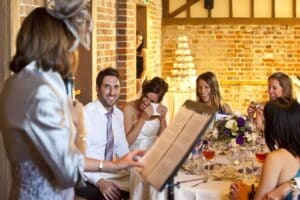 Mother delivering wedding speech, bride crying with joy and groom smiling.
