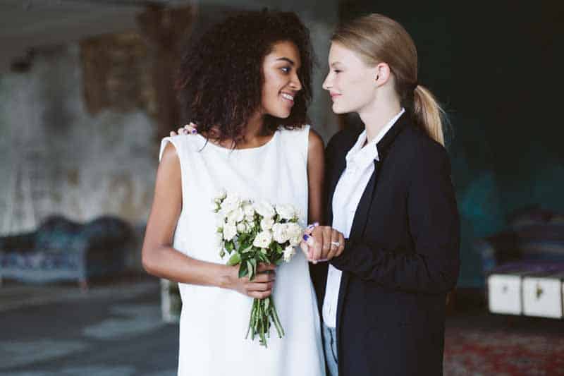 Lesbian brides holding hands and looking into each others eyes.