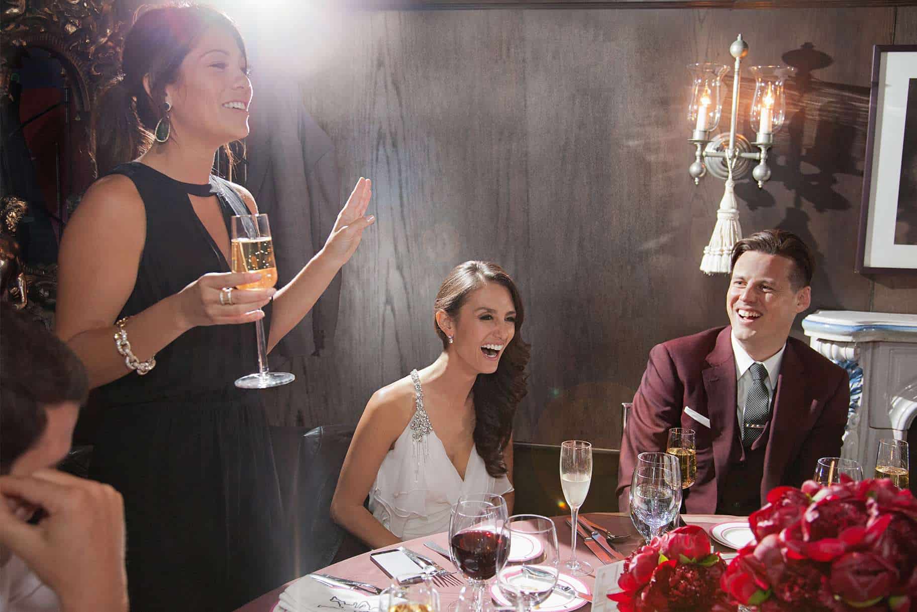 Sister of groom delivering a wedding speech with guests laughing.