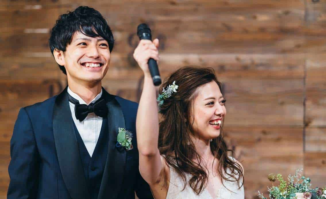 Bride and groom delivering a joint wedding speech. The bride is holding the microphone high in a triumphant pose.