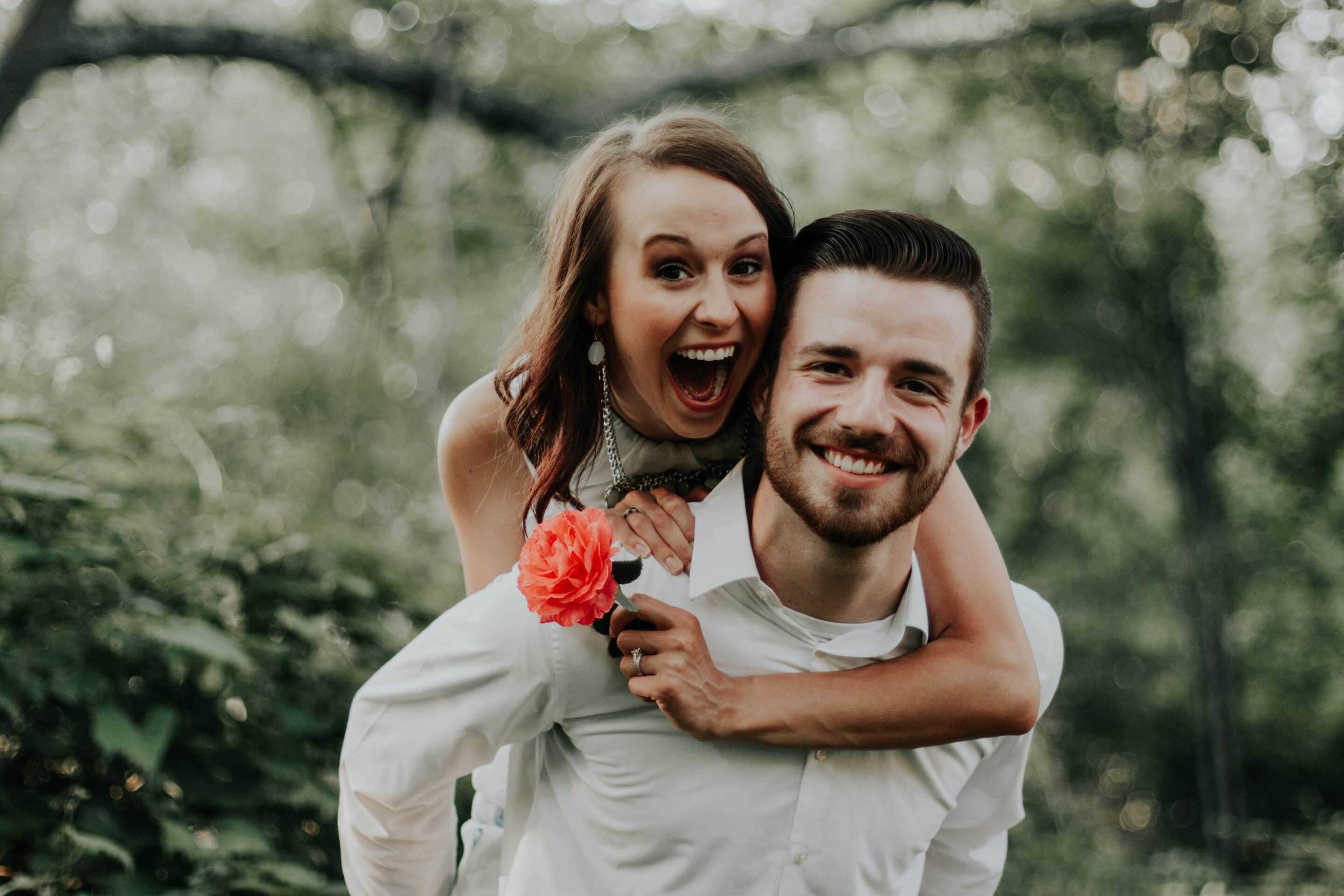 Bride being carried by groom. They are both smiling and she is carrying a rose.